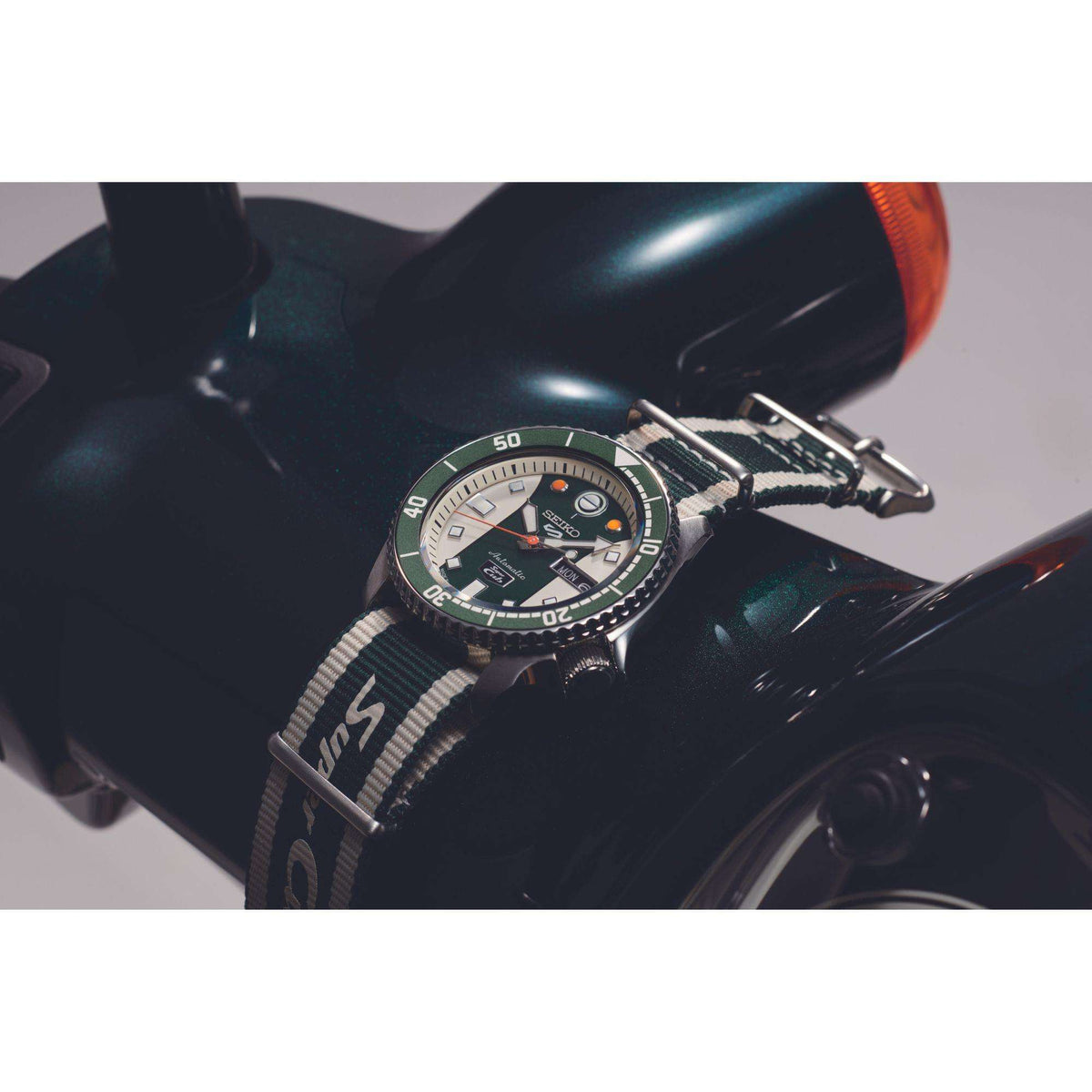 Green-dial automatic watch with striped fabric NATO strap on dark handlebar