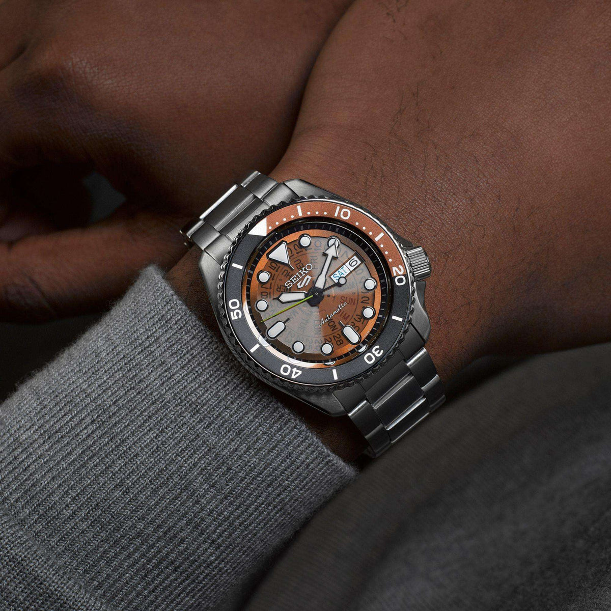 Men’s stainless steel skeleton dial watch on wrist, orange-brown dial, black bezel, date window