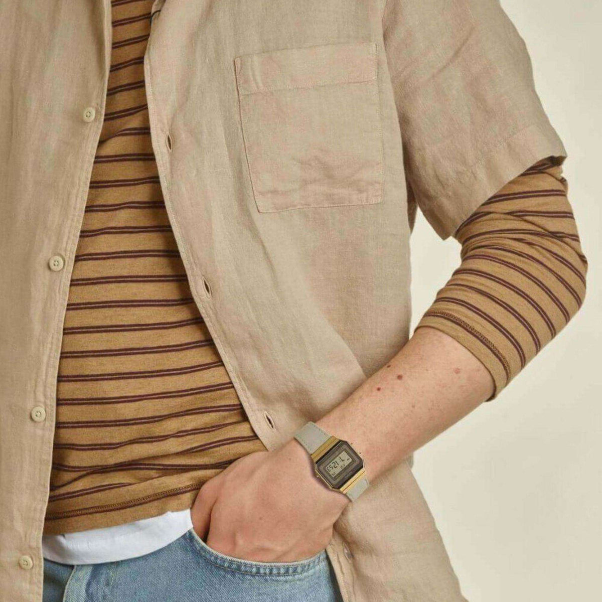 Digital watch on wrist with cream fabric strap and gold square case