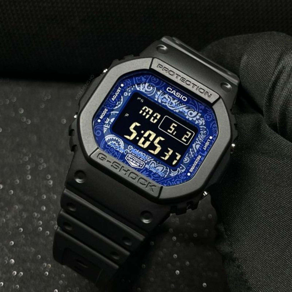 Casio G-Shock watch close-up showing blue patterned LCD, dark case, and digital time