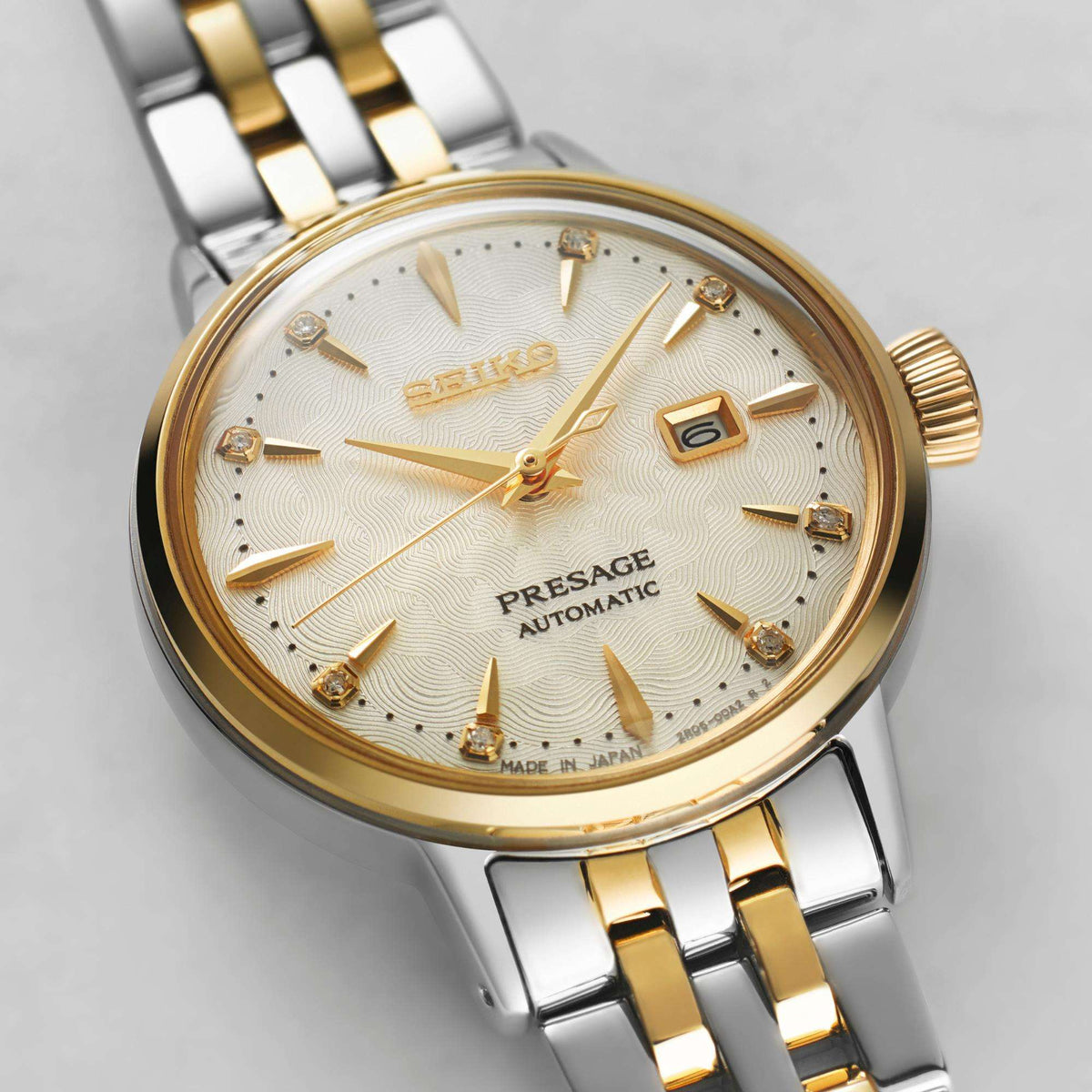Close-up view of the cream dial, highlighting its textured, sharp gold hands, framed date window, and diamond indices.