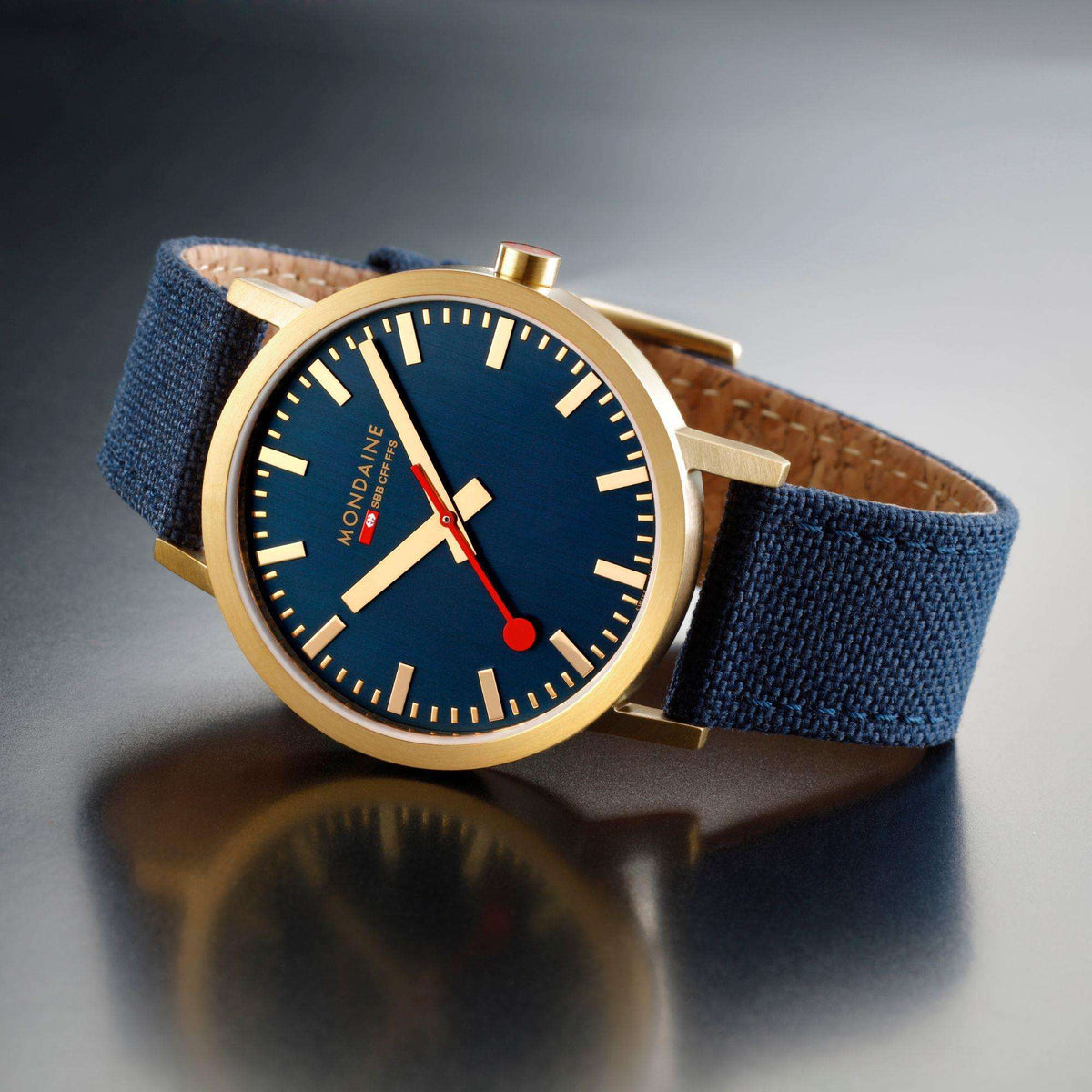 Mondaine Classic watch on dark background with navy-blue dial, gold-tone case, blue strap