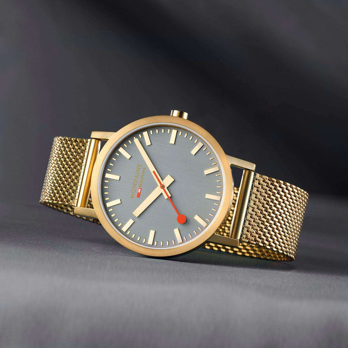 Gold-tone mesh watch on dark background, grey dial with red seconds and baton markers