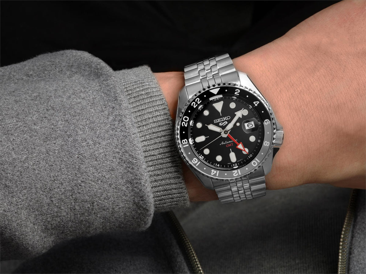 Men's black dial GMT watch on wrist with steel bracelet and black bezel, red GMT hand accents