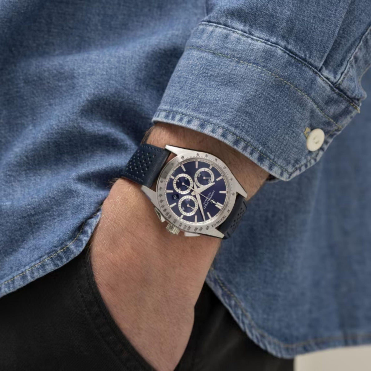Men's automatic chronograph watch on wrist, dark blue dial, navy leather strap, silver tachymeter.