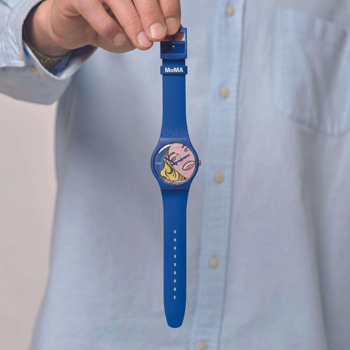 Blue silicone strap Swatch wristwatch held by hand; pop-art girl dial