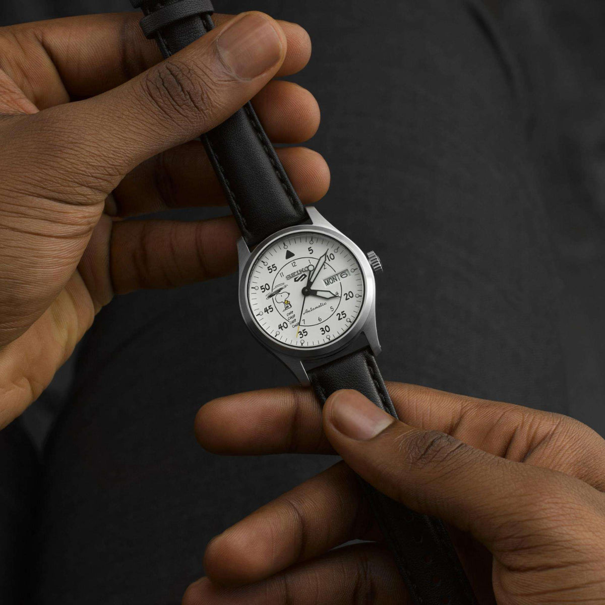 Automatic watch held in hand, black leather strap and white dial visible