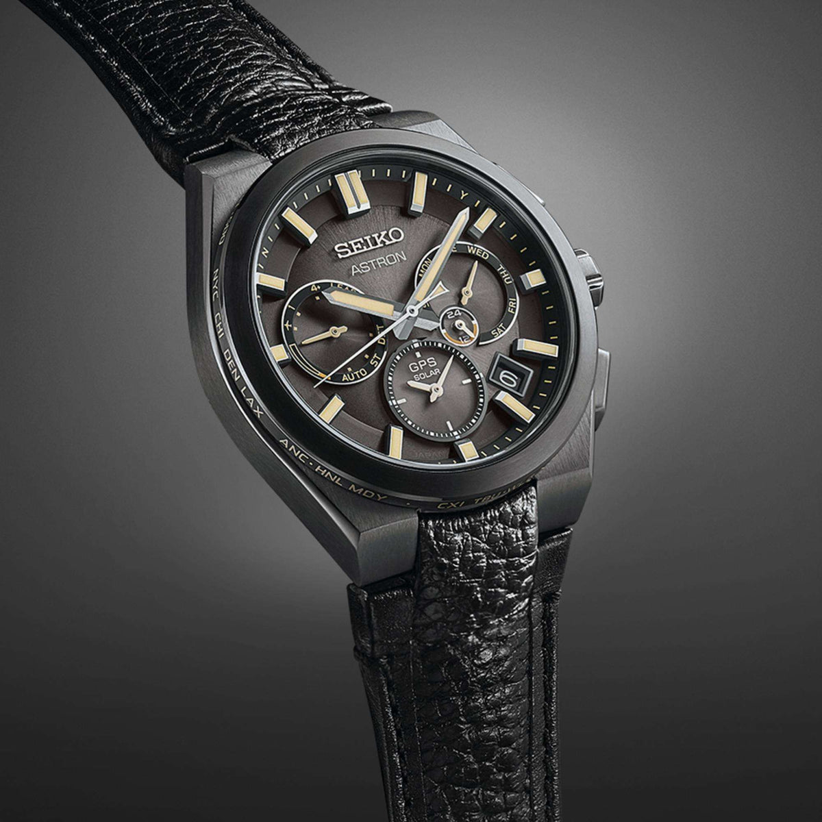 Angled view of the watch against a dark gradient backdrop, accentuating the black titanium bezel and the leather strap.