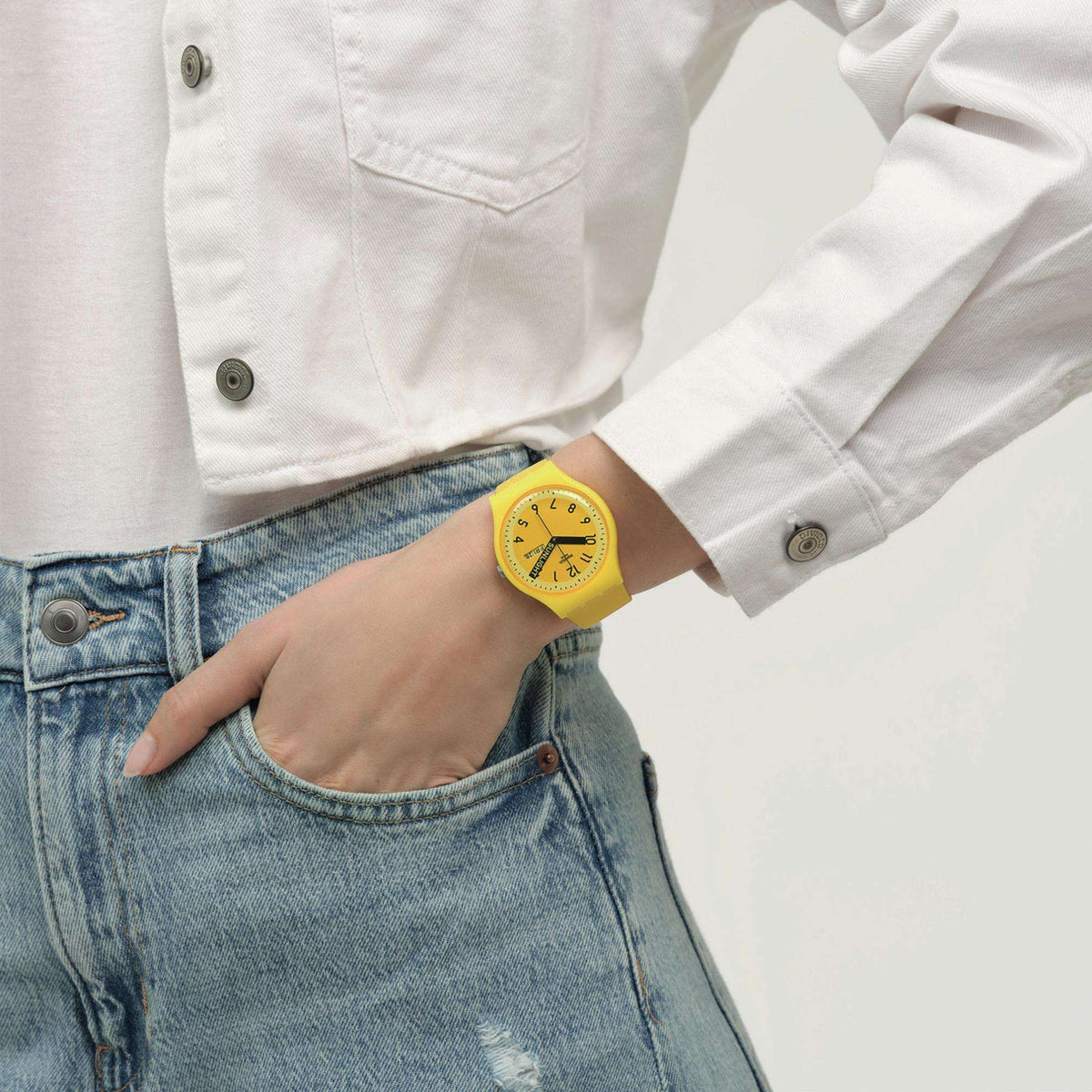 Yellow quartz wristwatch on wrist with yellow dial, worn with denim jeans and white shirt