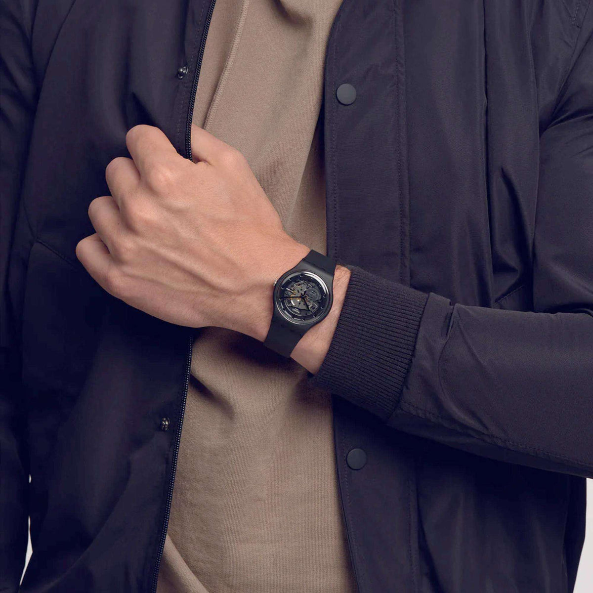 Quartz watch on wrist with dark rubber strap and skeleton dial, worn with blue jacket sleeve