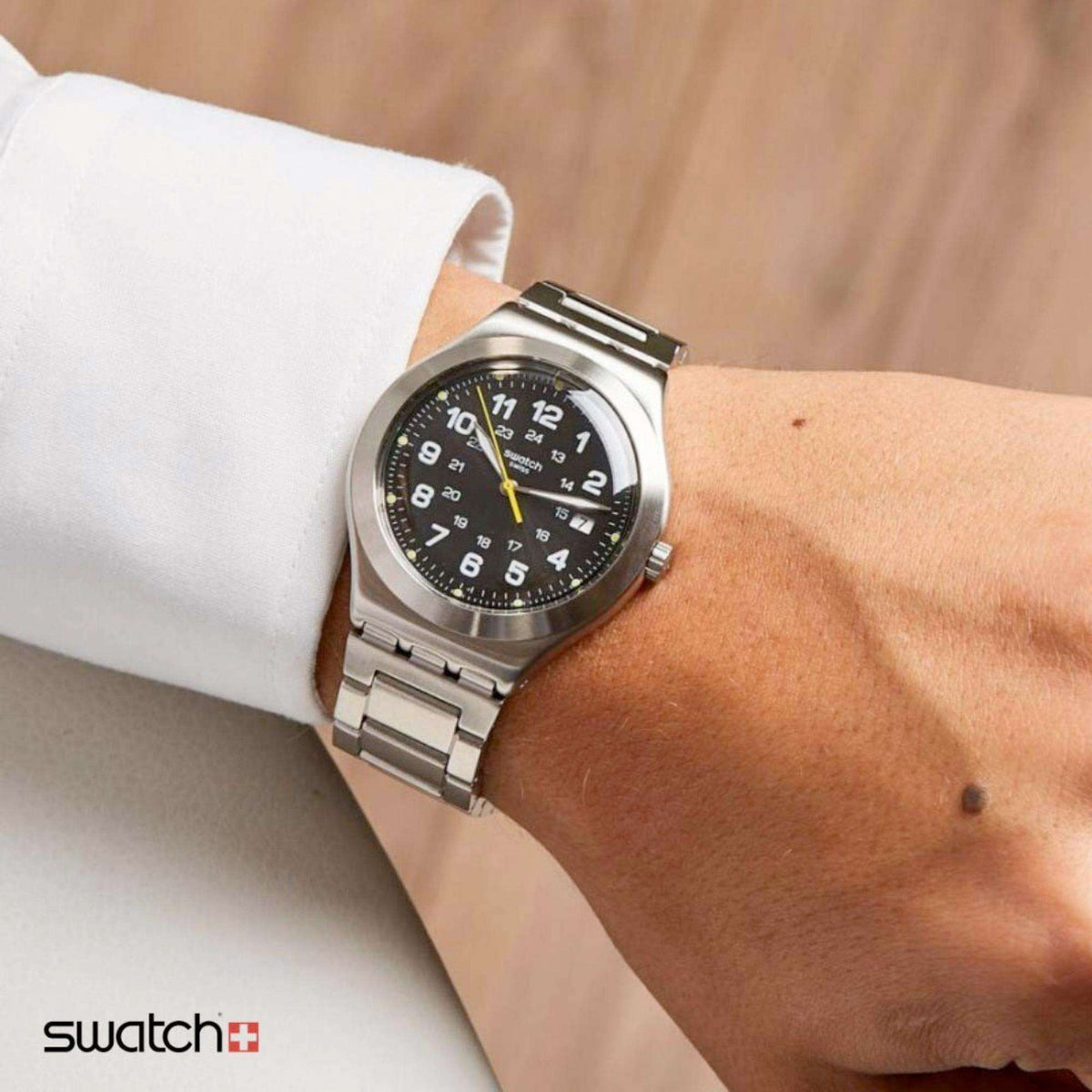 Stainless steel quartz wristwatch on a wrist with black dial, yellow hands, and metal bracelet.