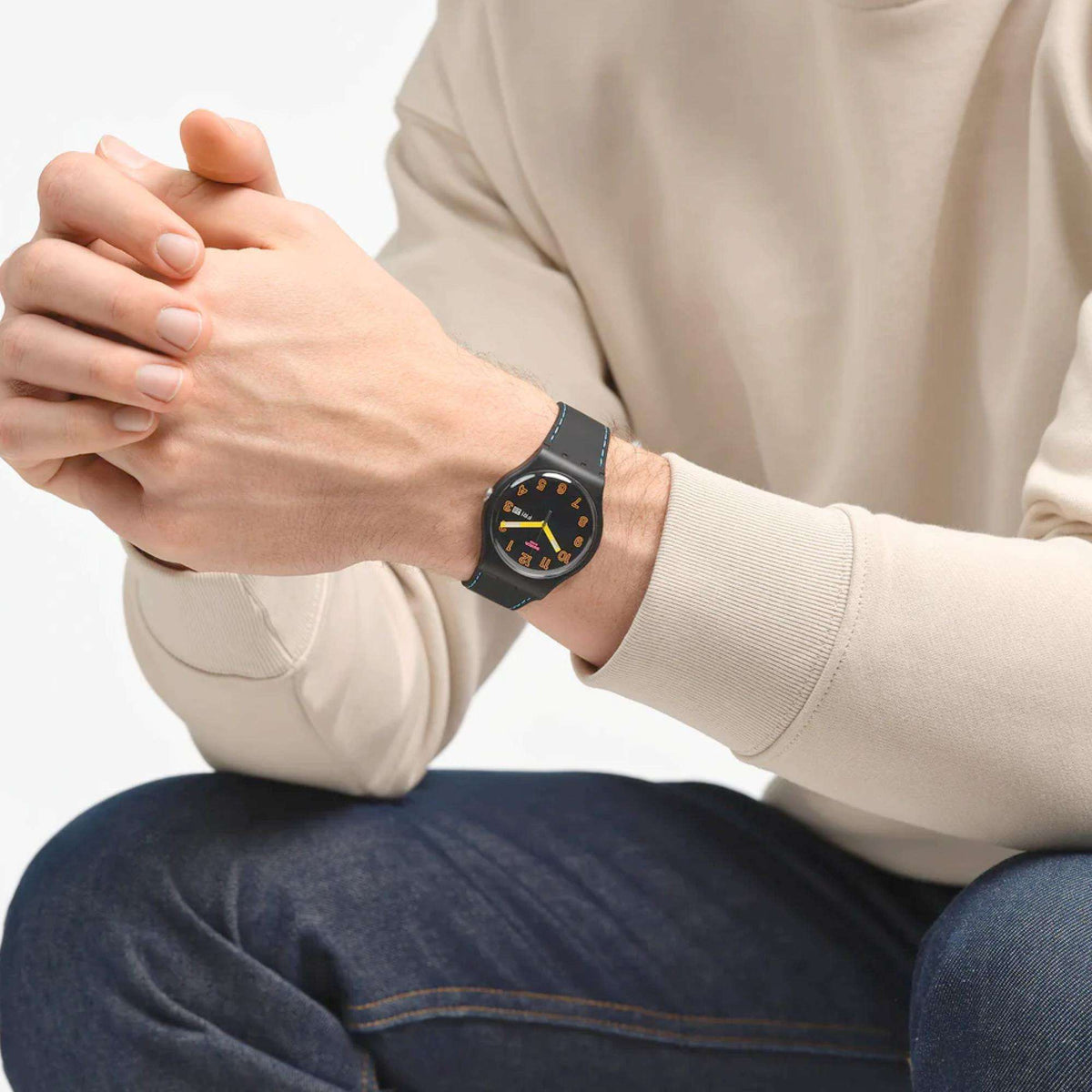 Quartz wristwatch on a person’s wrist, round black dial with yellow hands and blue-stitch strap