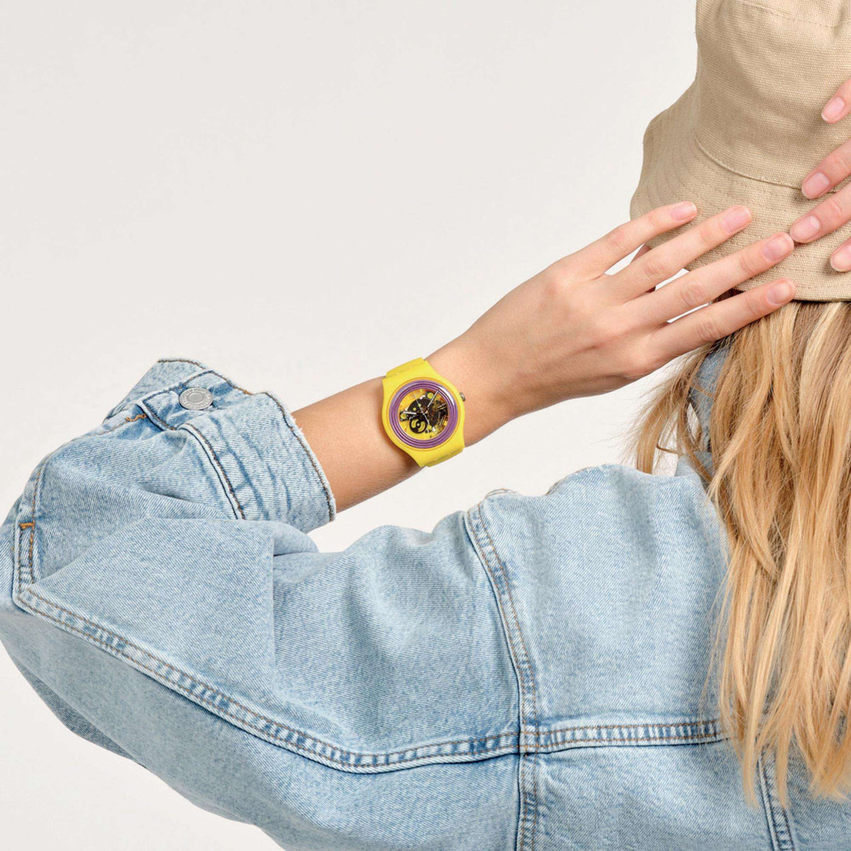 Yellow wristwatch with purple ring dial worn on denim-clad arm