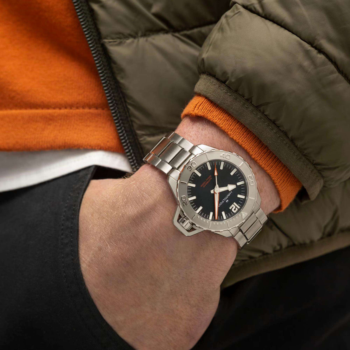 Wrist-worn men’s steel automatic watch with black dial and orange hands