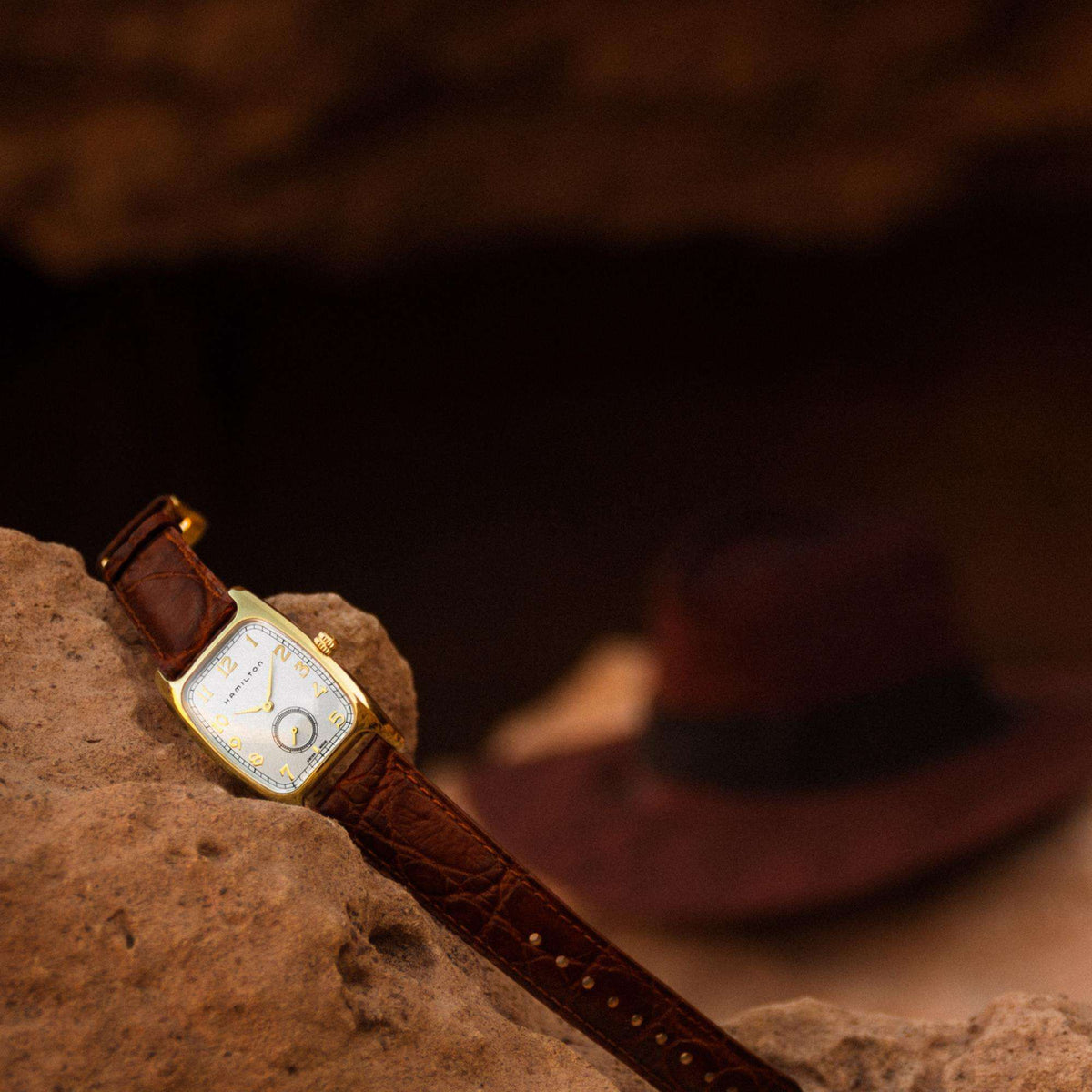 Hamilton American Classic Boulton H13431553 Indiana Jones watch displayed on stone with signature fedora hat blurred in background