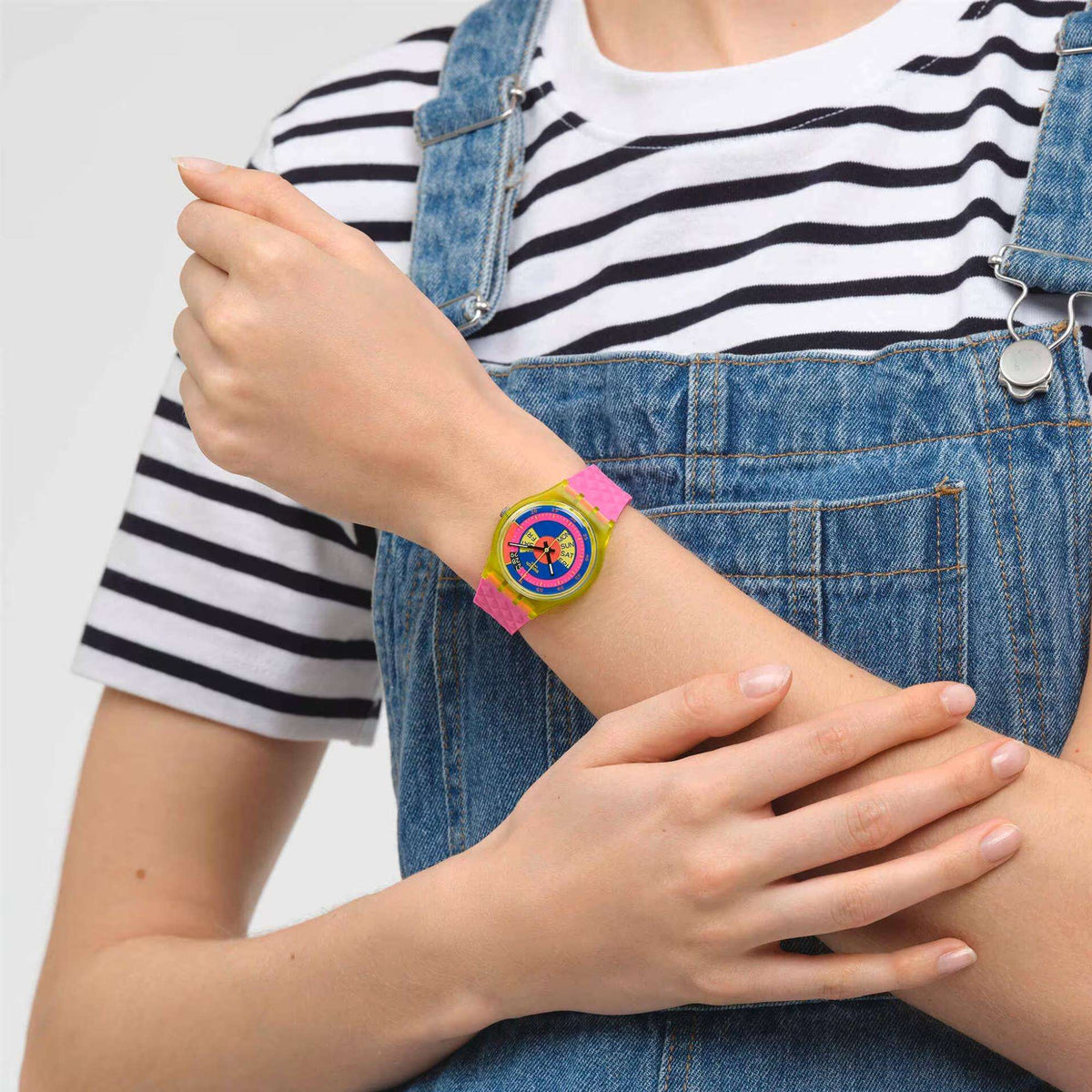 Swatch neon ladies watch on wrist: bright pink strap and colorful rainbow dial