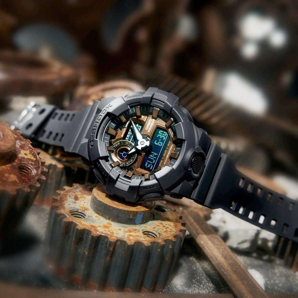 Men's black G-SHOCK digital watch, gold bezel details, chunky resin strap; side buttons visible.