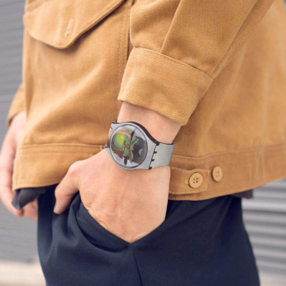 Swatch wristwatch on wrist with art dial and light gray strap under a tan jacket