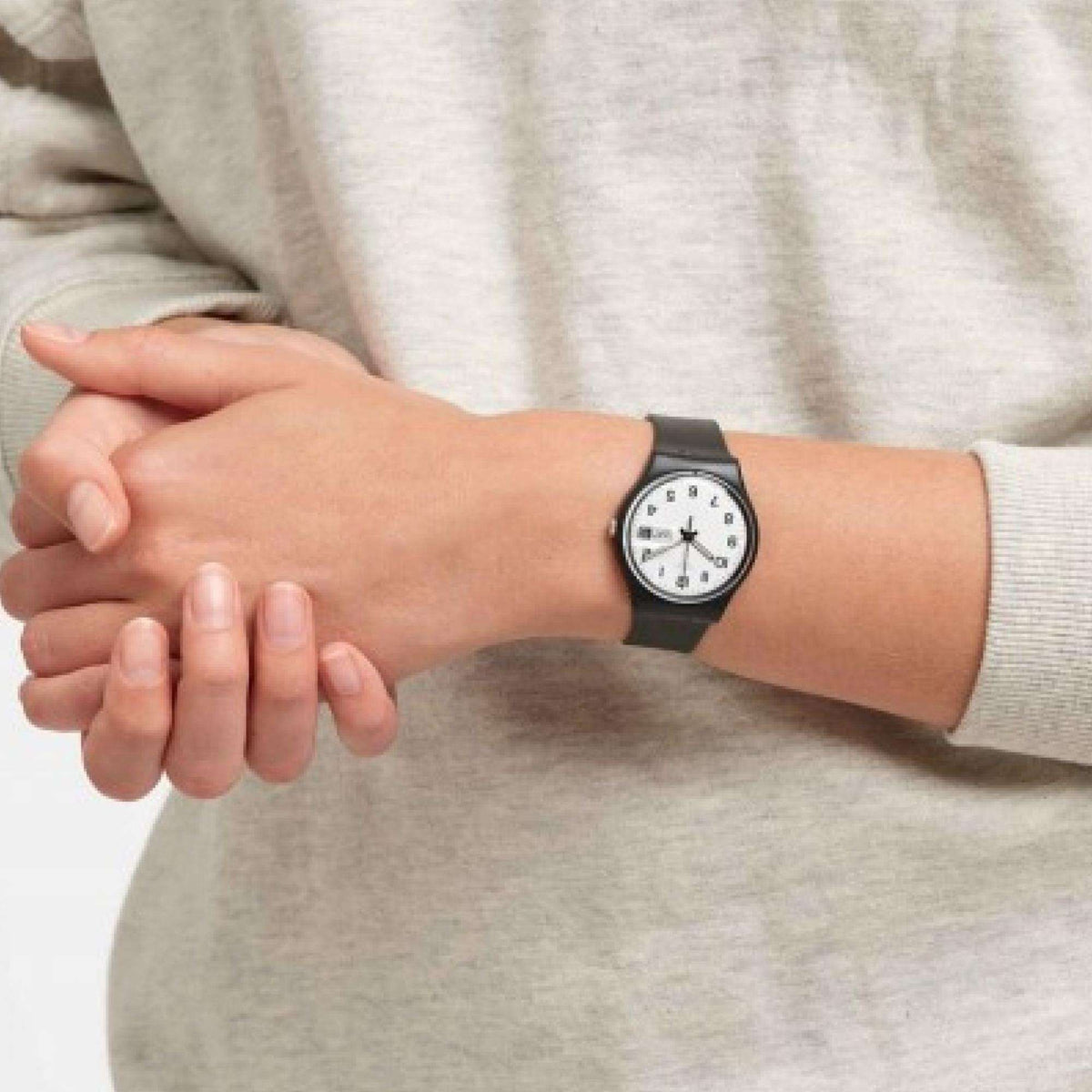 Hand wearing a black silicone strap wristwatch with white dial and date window