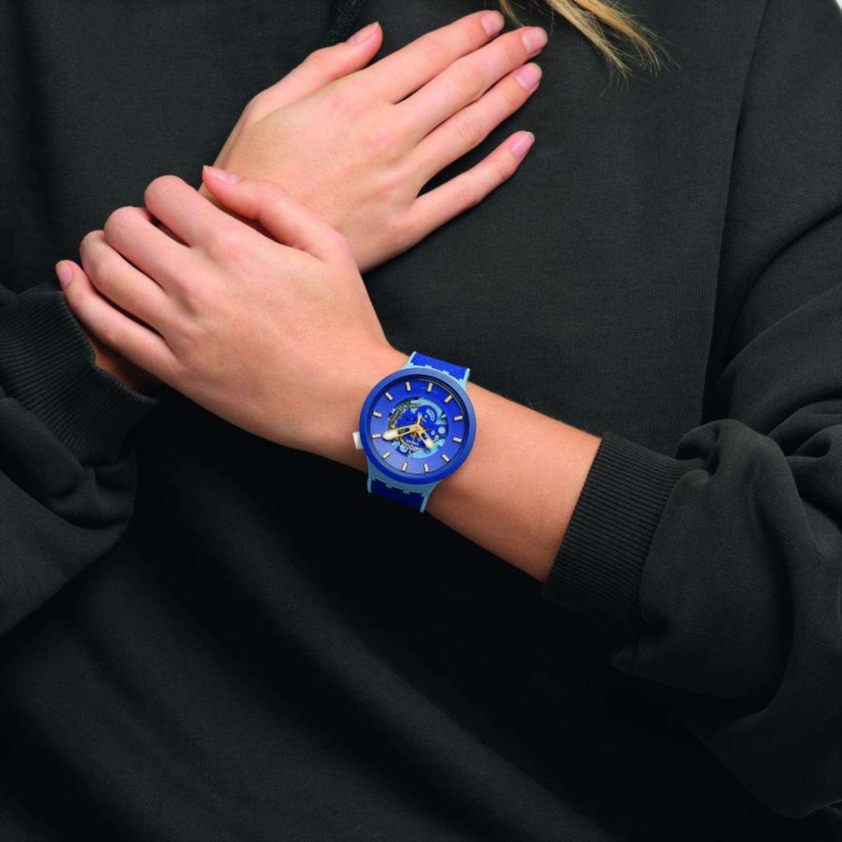 Blue wristwatch worn on wrist against dark clothing, showing blue dial and band