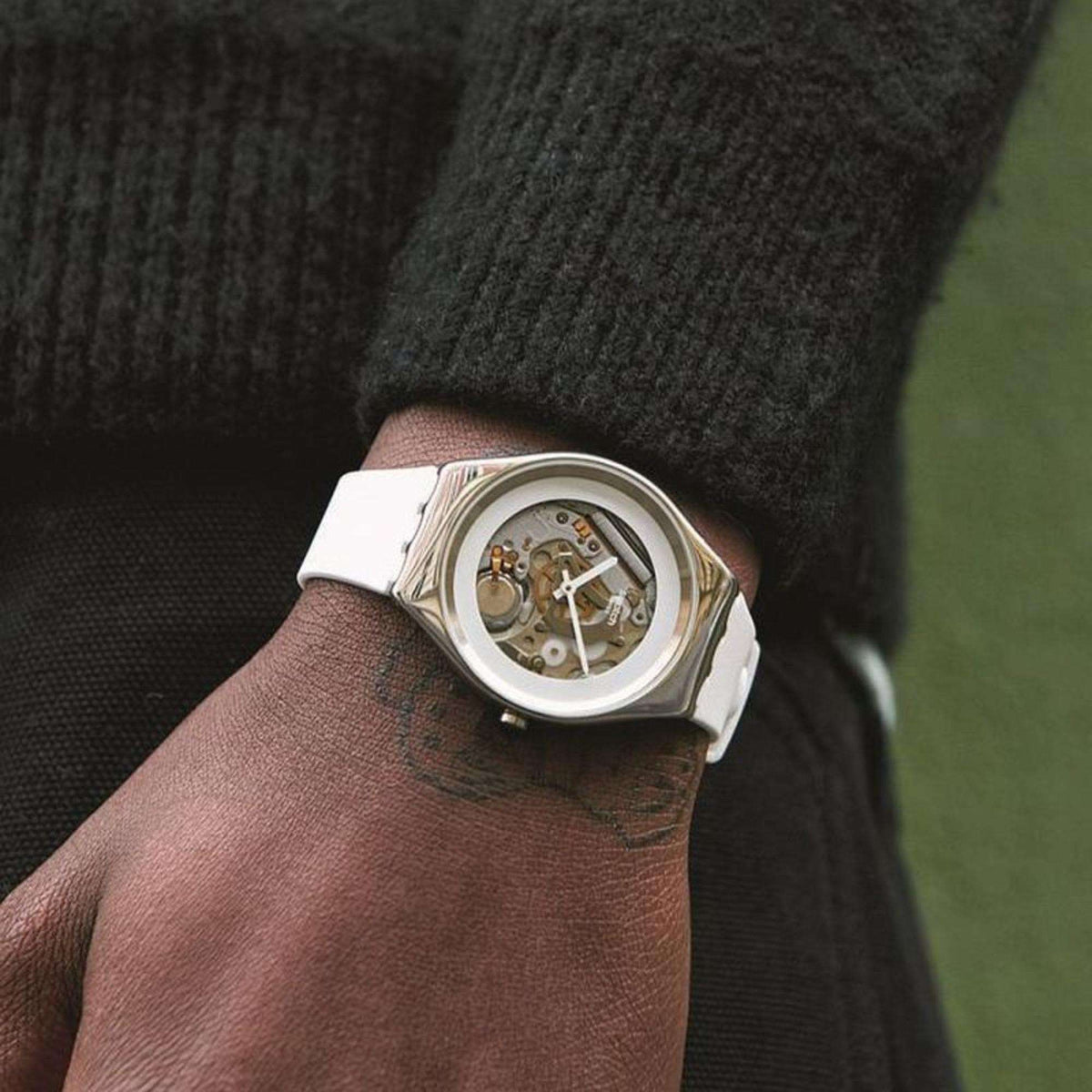 Men's wristwatch: silver case, skeleton-style dial, white strap.