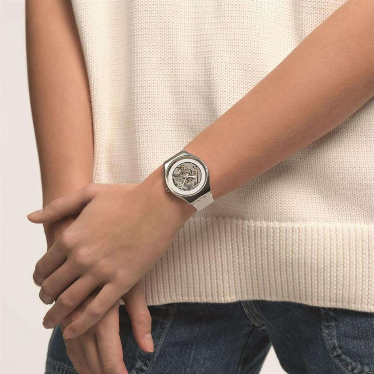 Men's wristwatch on wrist with silver case, skeleton dial, and white strap.