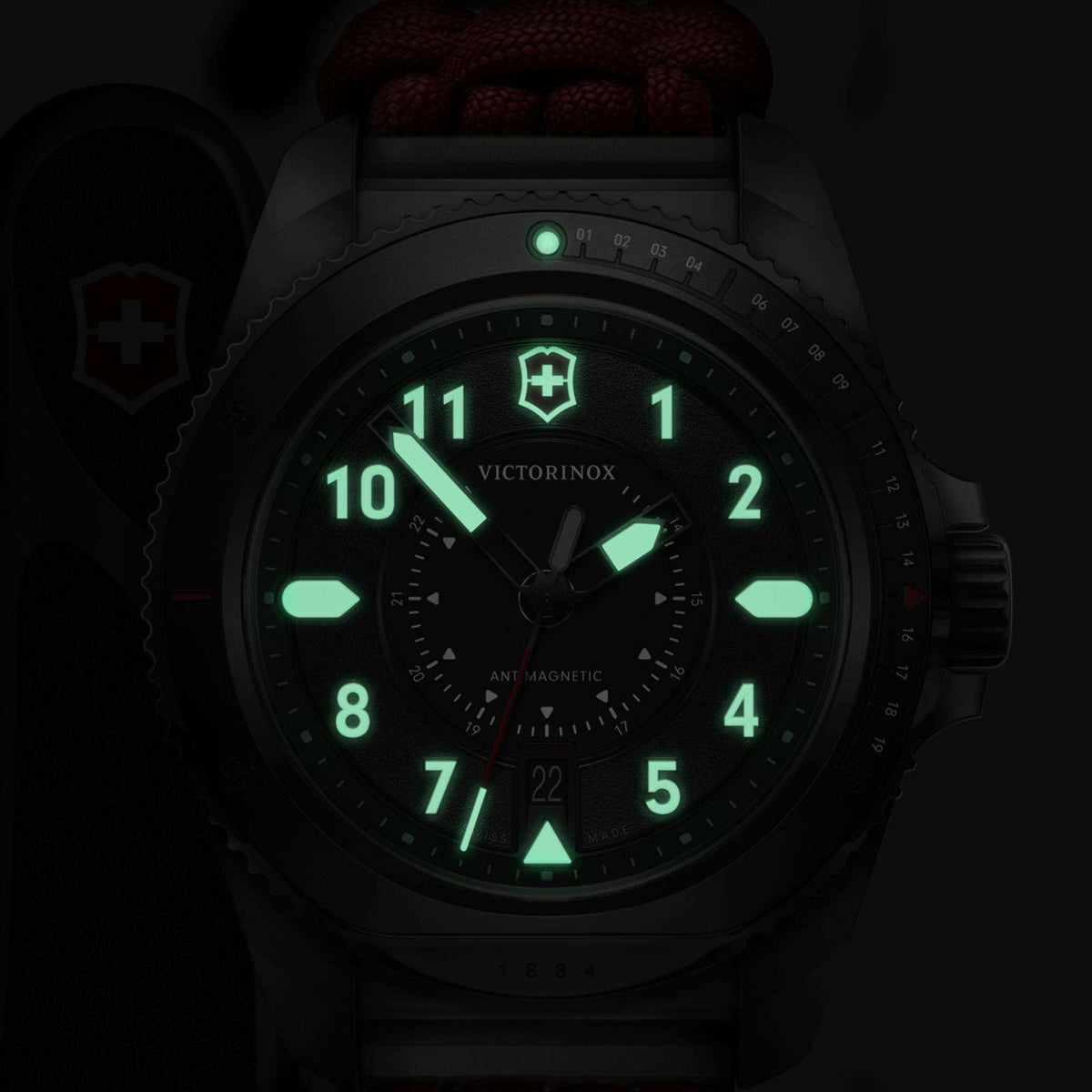 Men’s quartz watch with black dial and green luminous hour markers; steel case, red paracord.