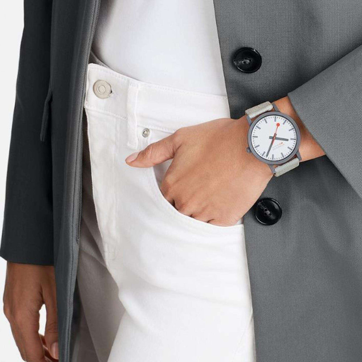 Unisex watch on wrist with white dial, red second hand, and grey textile strap.