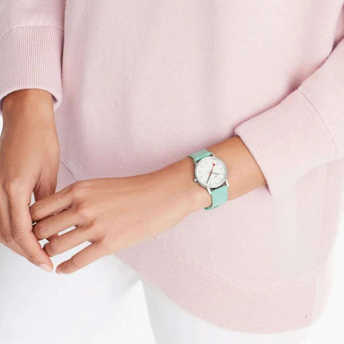 Green textile-strapped ladies quartz watch on wrist with pink sweater sleeve