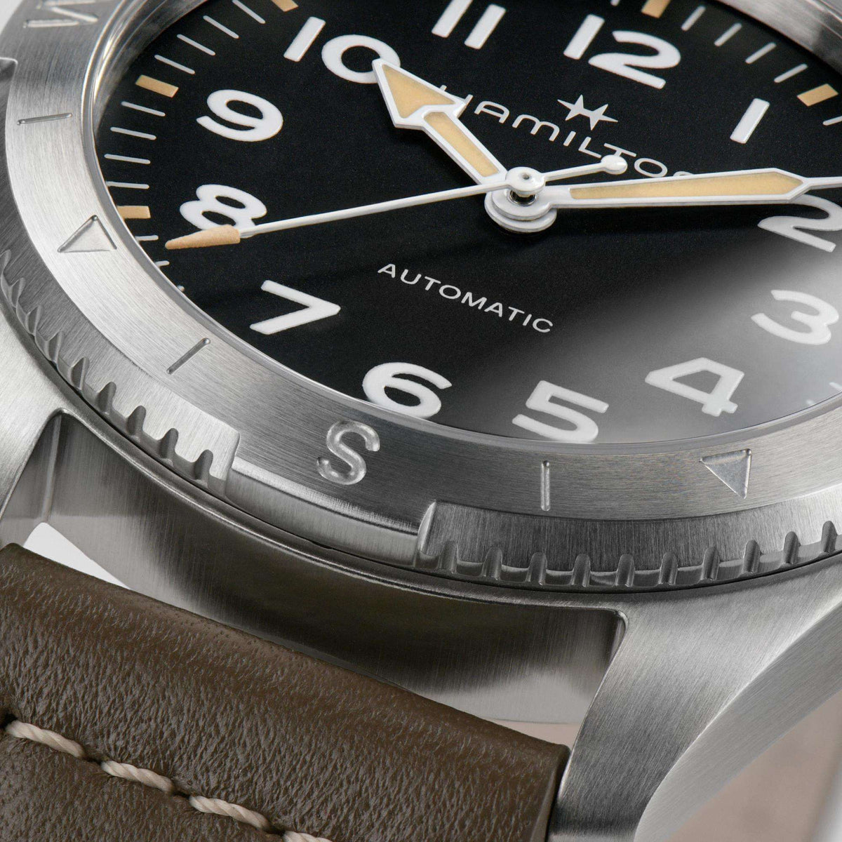 Men's automatic wristwatch close-up: black dial with gold hands, numerals, and metal bezel.