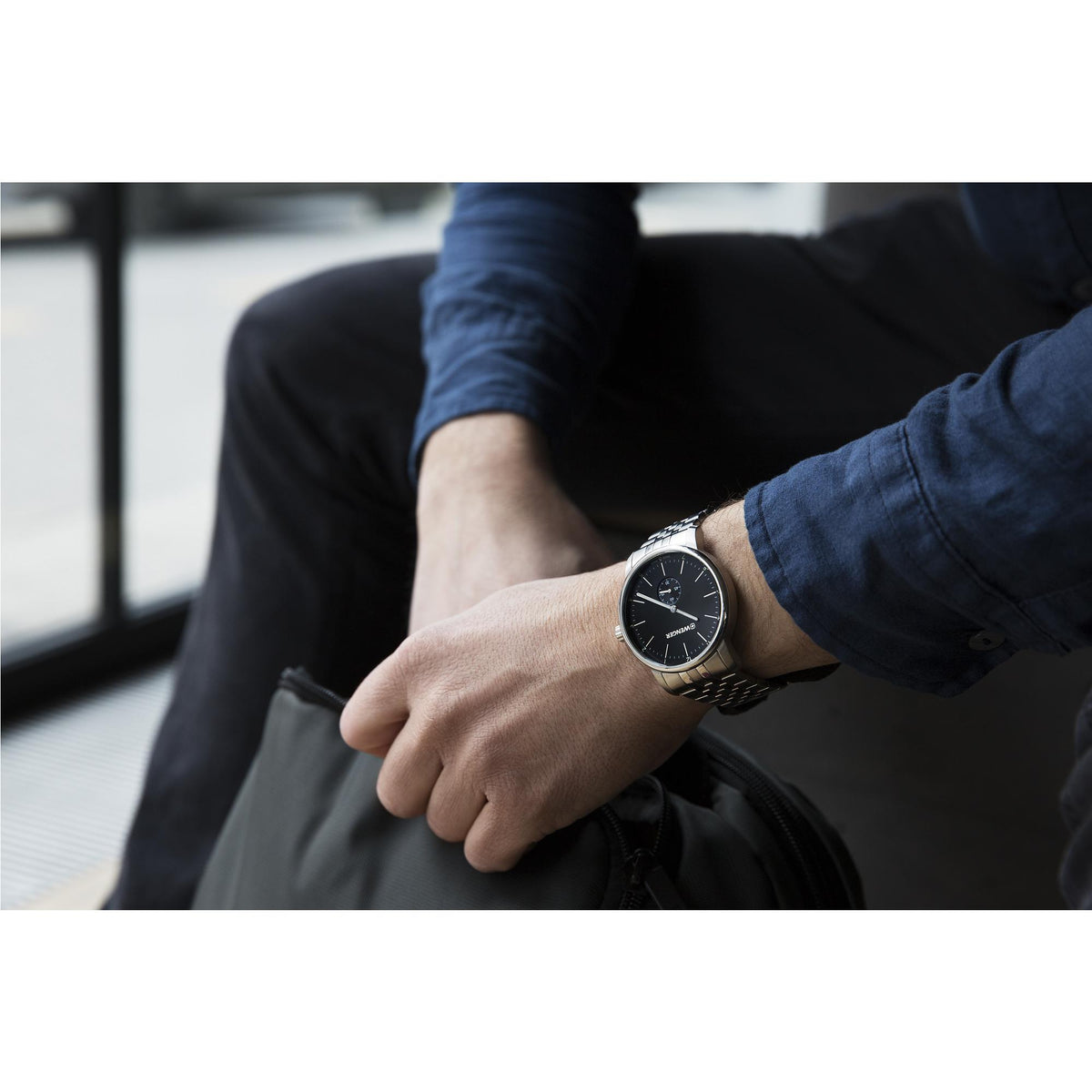 Wristwatch on seated arm: black dial with minute markers and stainless steel band.
