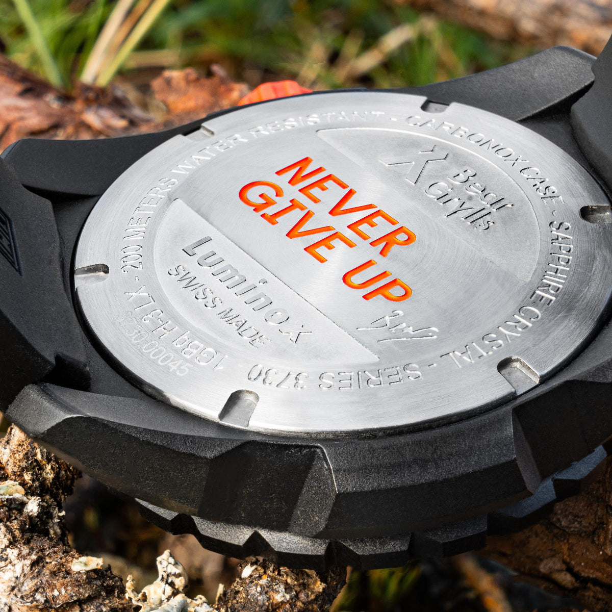 Engraved watch case back with “NEVER GIVE UP” text and orange strap piece