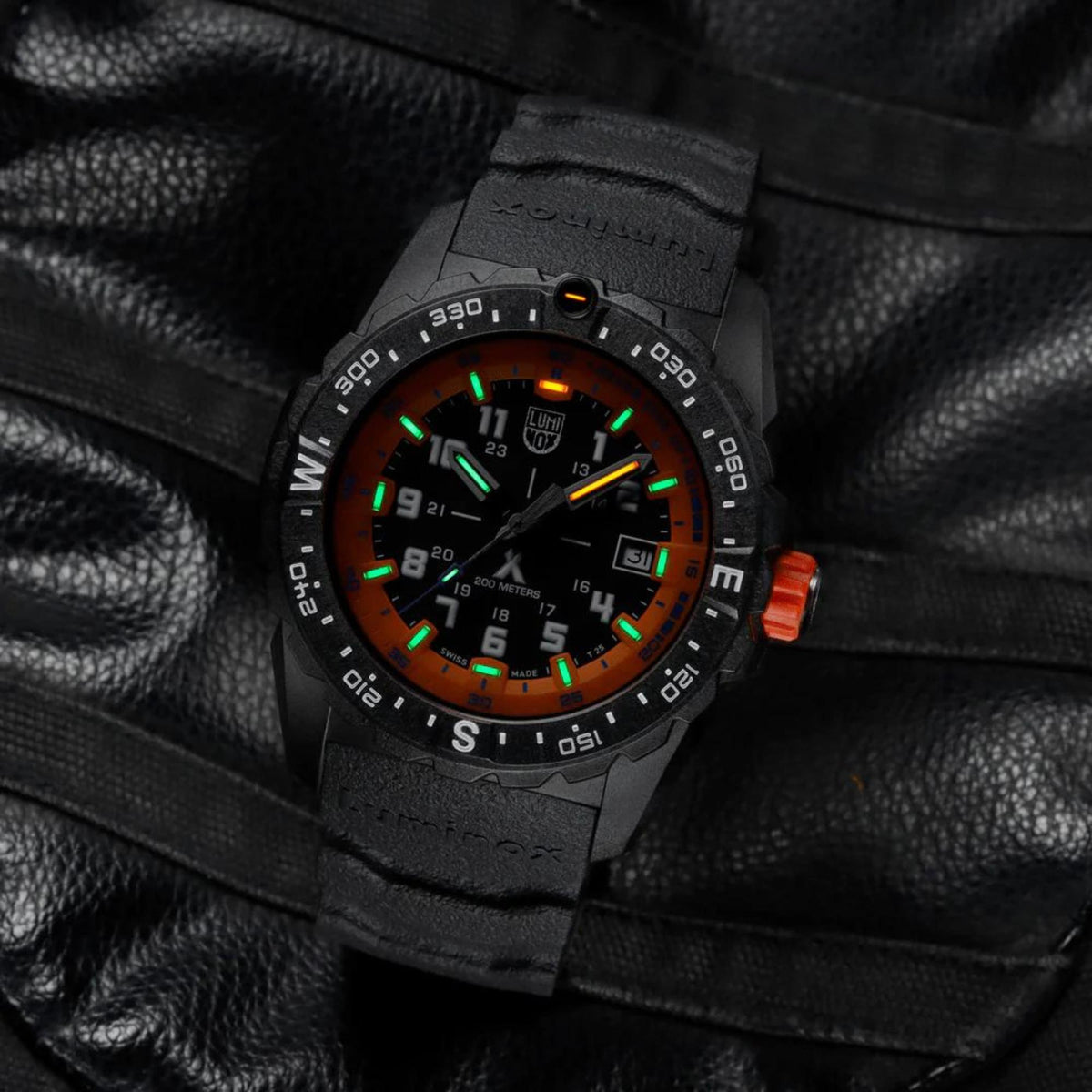 Black rubber men’s watch on leather with orange dial and green glowing hour markers.
