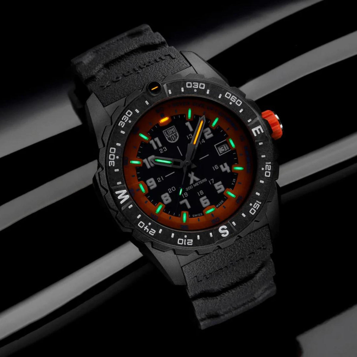 Black rubber quartz watch with orange dial and green glowing markers in dark lighting.