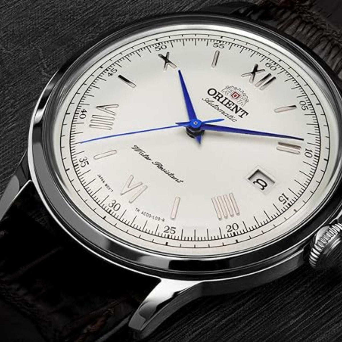 Orient Bambino TAC00009W0 watch close-up displaying metallic blue hands, Roman numerals, and date window on a white dial