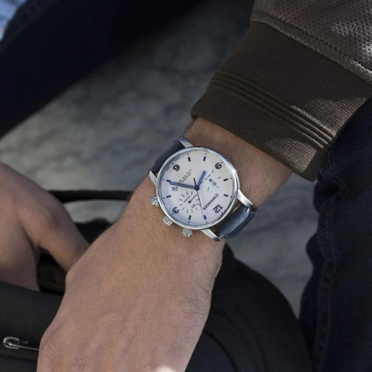 Men's wristwatch on dark sleeve: cream dial chronograph, blue leather strap, silver case