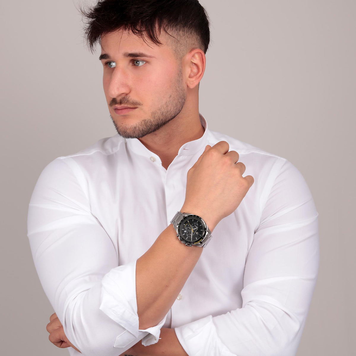 Men's watch worn on wrist: black chronograph dial, yellow accents, stainless steel bracelet.