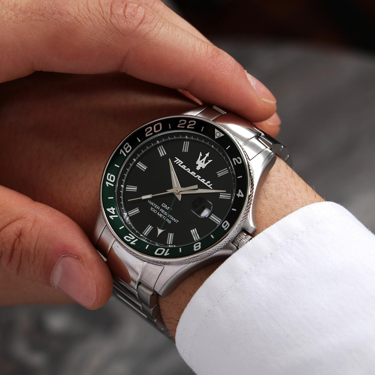 Maserati GMT quartz watch on wrist with black dial, green bezel, and steel bracelet.