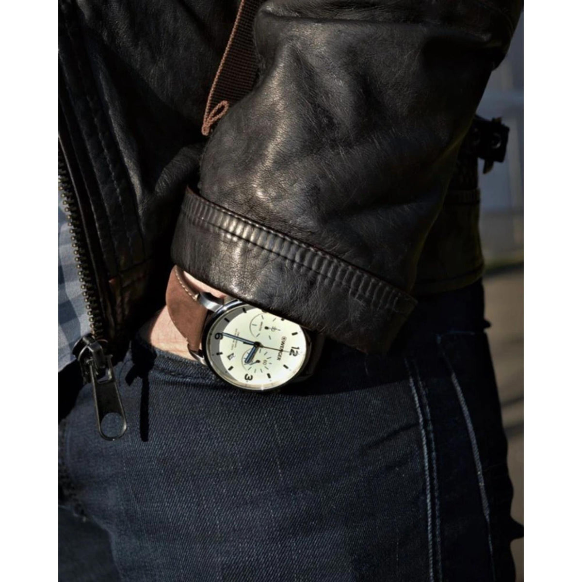 Chronograph watch on brown leather strap over denim; cream dial with blue hands