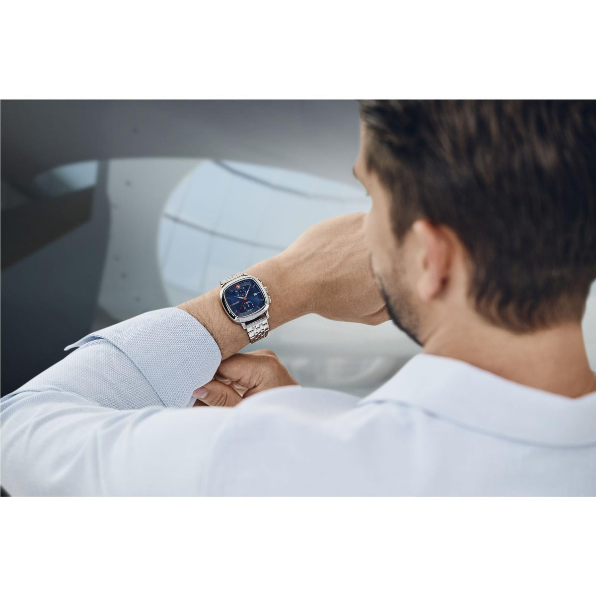 Stainless steel watch on man’s wrist, dark blue face with red seconds and subdials