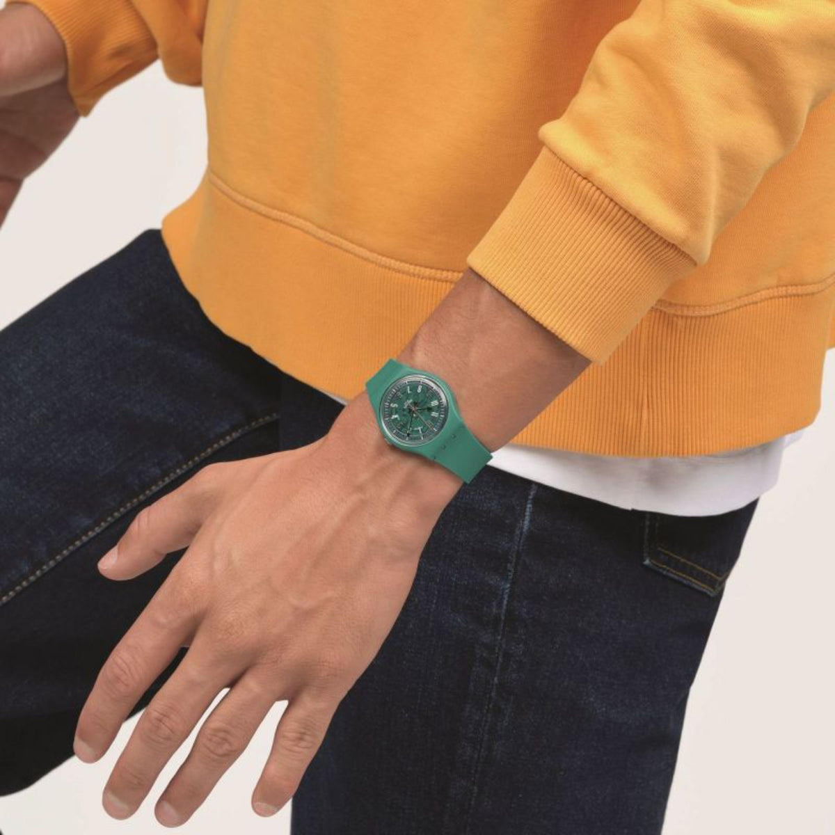 Turquoise silicone skeleton dial watch on wrist with dark hands, worn with orange sleeves