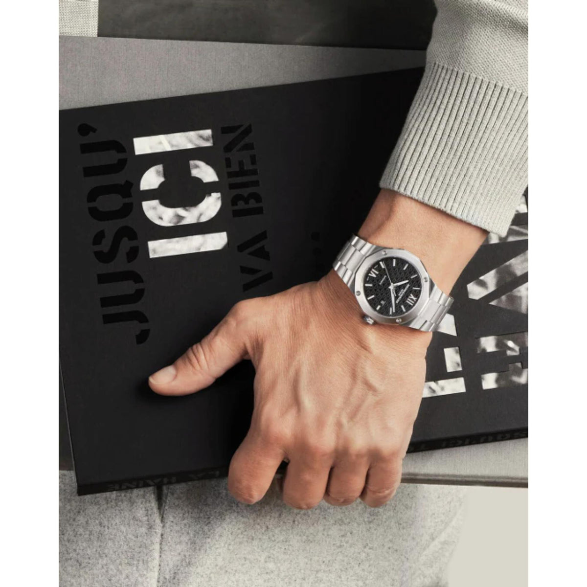 Men's stainless steel watch worn on wrist, black dial with Roman numerals