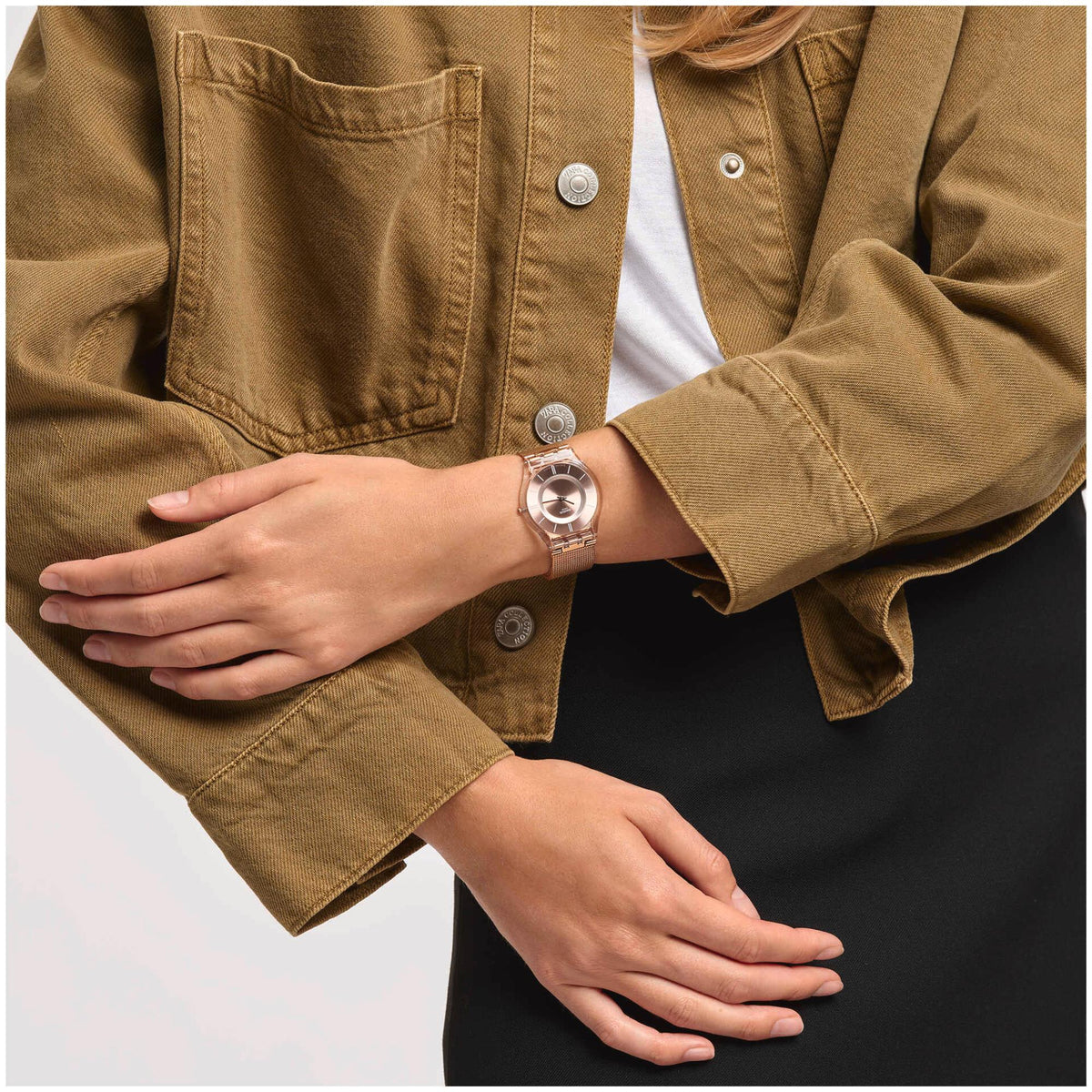 Rose gold-toned watch with pink dial worn on wrist, visible with tan jacket sleeves