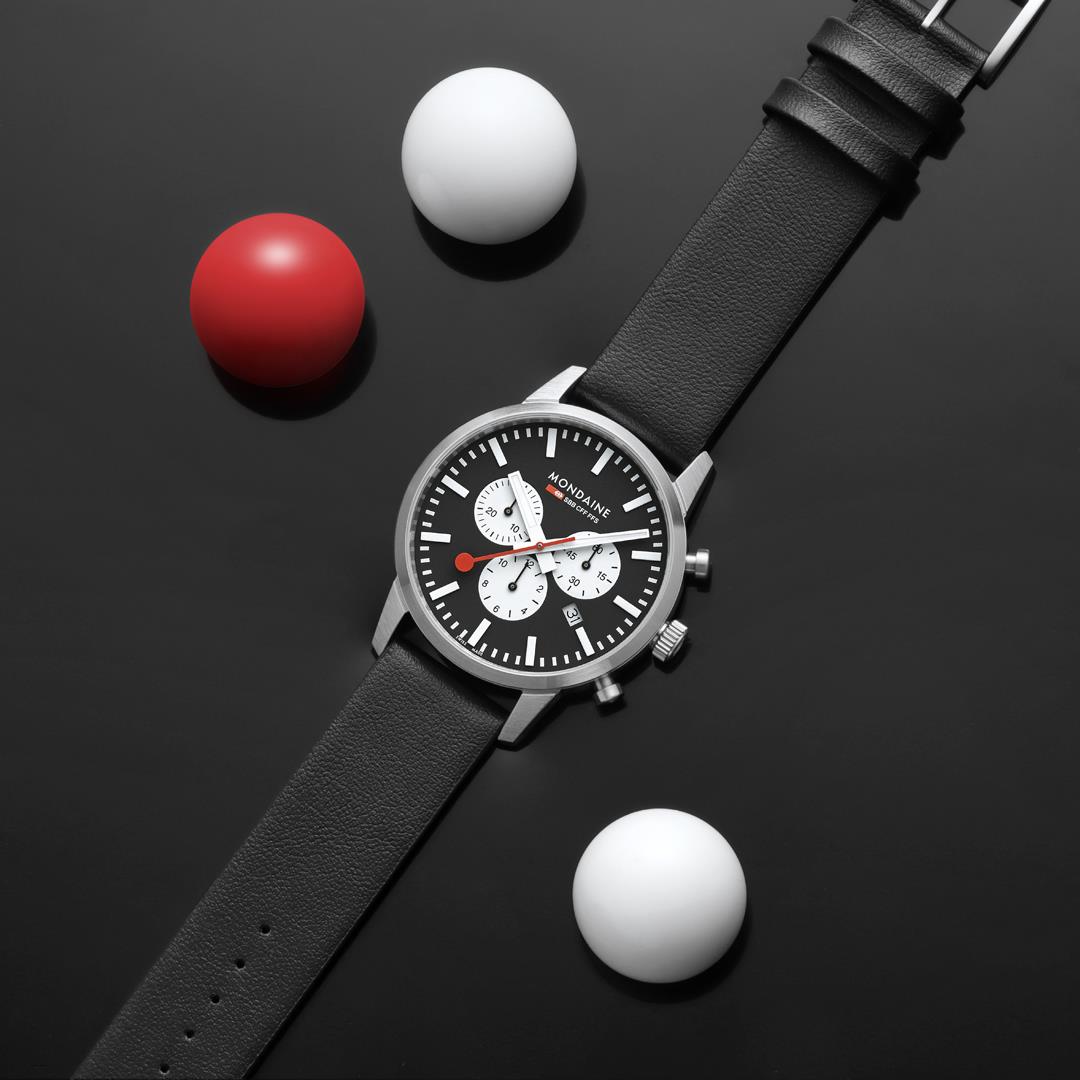 Mondaine Neo MSD.41420.LBV flat lay view displaying a black dial on a dark surface with decorative spheres