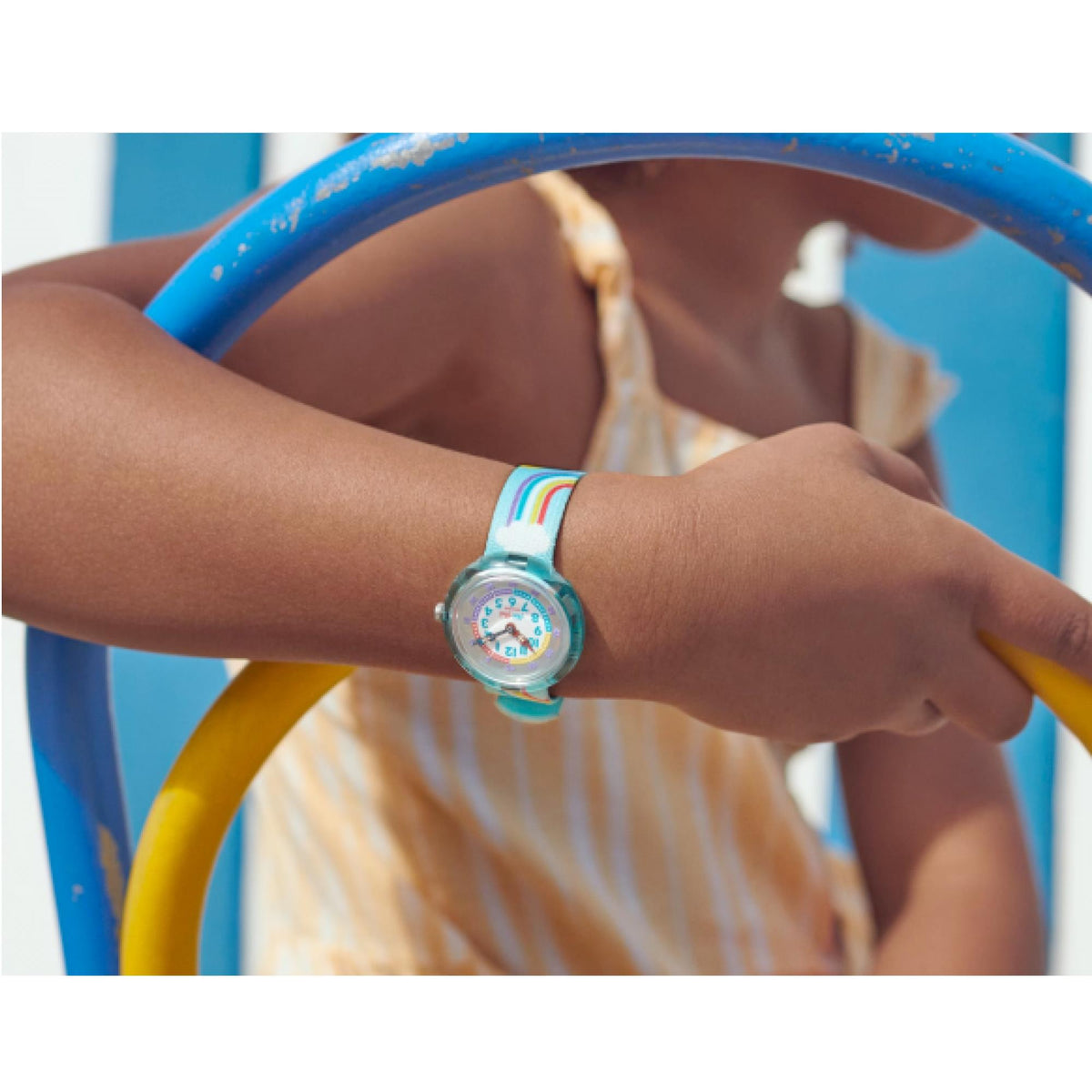 Kids wristwatch on arm, blue fabric strap with rainbow accents and round dial