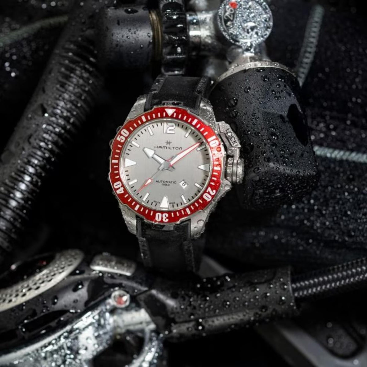 Automatic diver watch on black rubber strap with red bezel and grey dial; water droplets