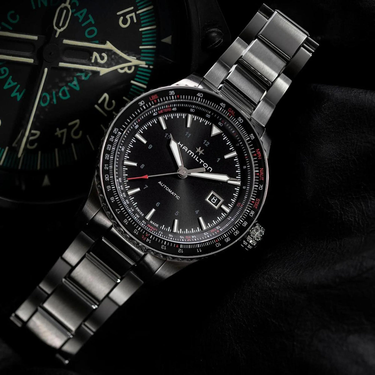 Angled shot of the Hamilton Khaki Aviation 42mm black dial steel mens automatic watch H76615130 positioned beside an aviation instrument panel on a dark background
