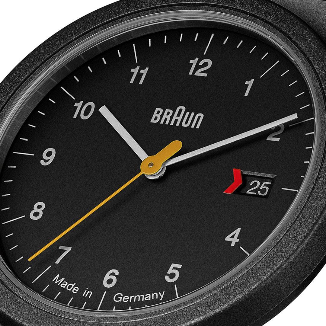 Close-up of black watch dial with yellow hands and red date window showing 25