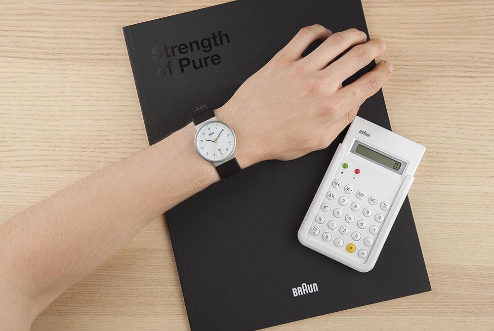 Men's watch worn on wrist with white dial and black leather strap, silver case