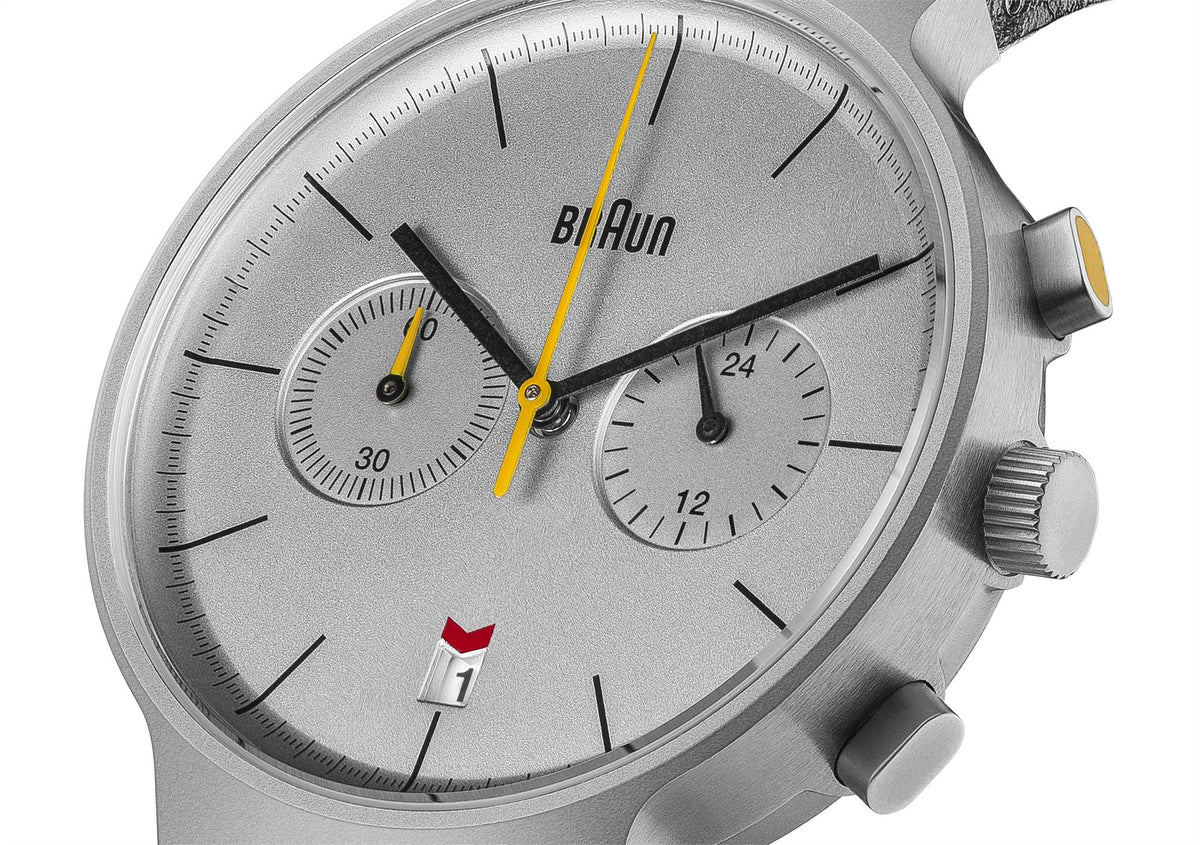 Close-up watch dial, silver face with black markers, yellow seconds hand, subdial at 3